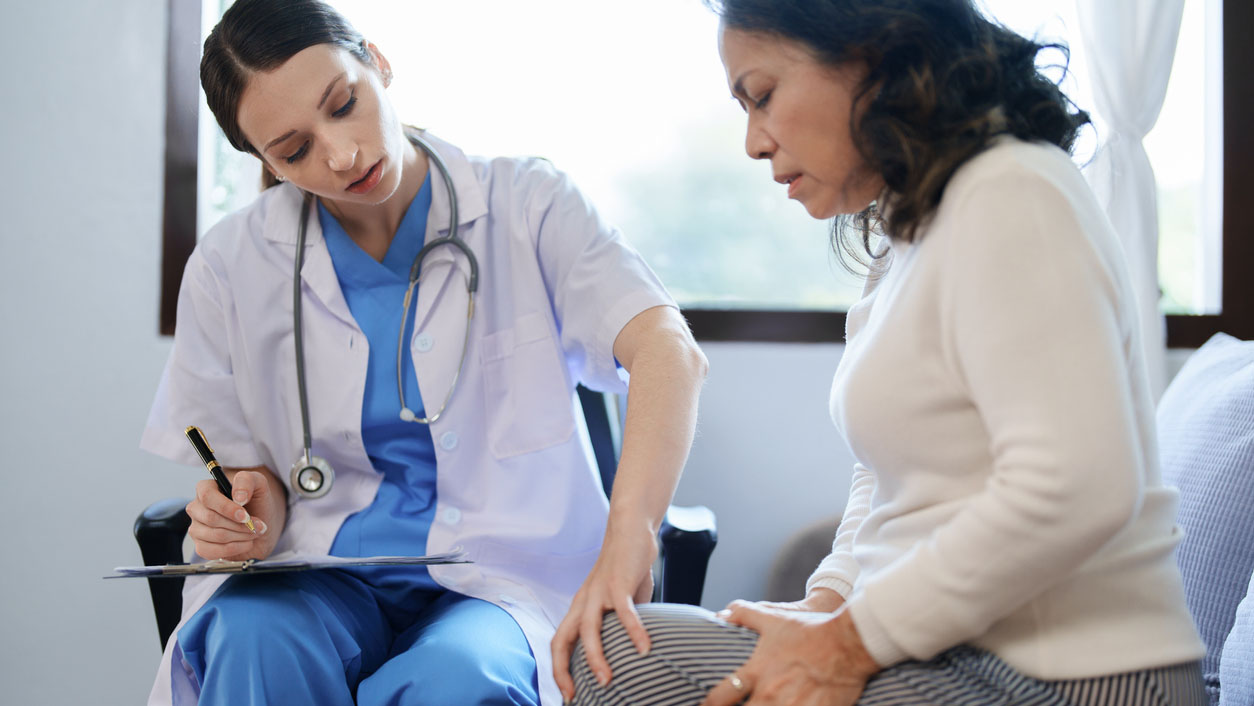 portrait of a female doctor talking to a patient with knee pain. Health care provider assessing a woman with knee pain.