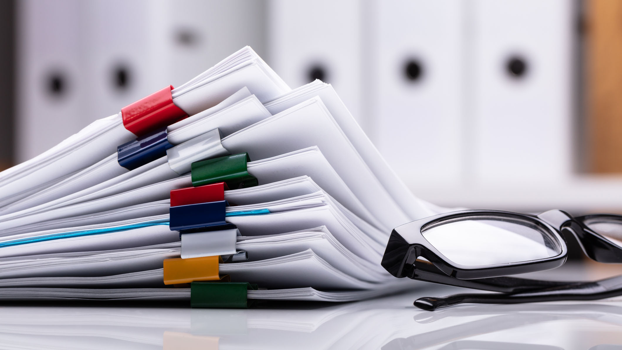 stacked documents and eyeglasses Stacked papers on desk next to reading glasses.