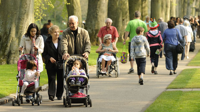 families and individuals walking on a park trail Crowded park of families walking amongst a flower garden.